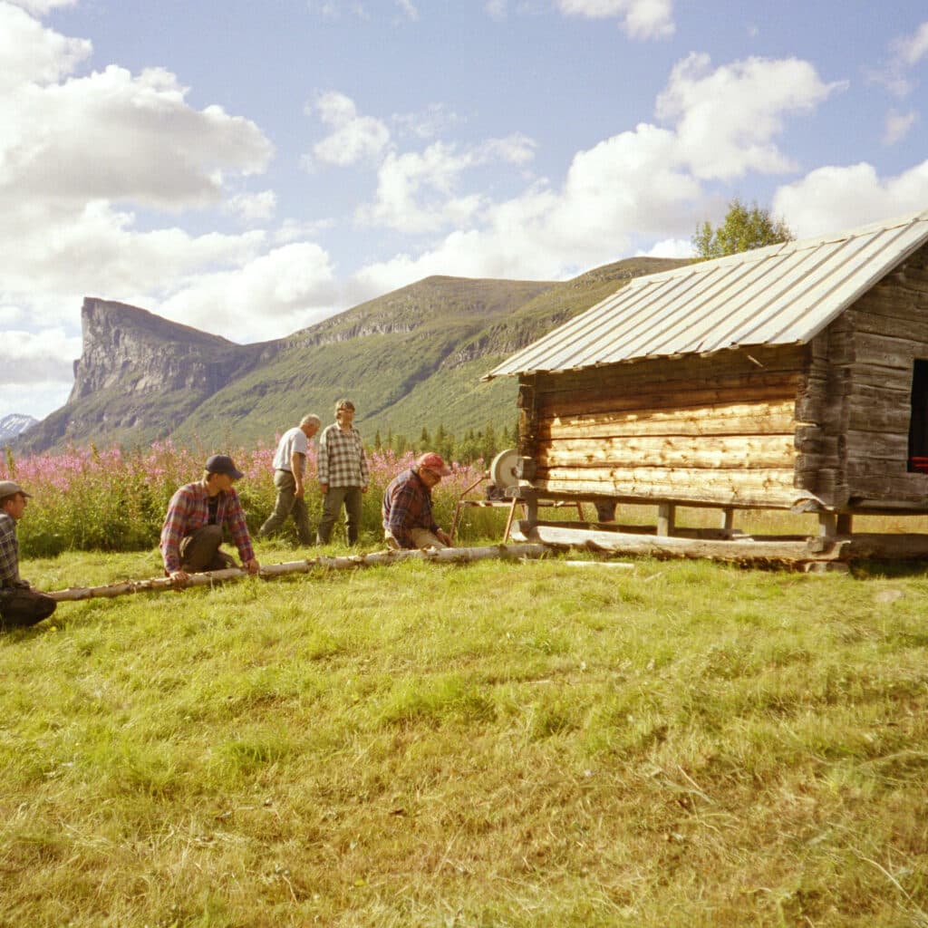 Skierfeklippan i bakgrunden. I förgrunden arbetar människor bredvid ett litet timmerhus