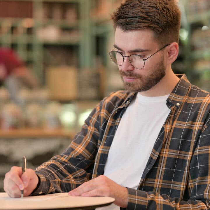 Till miljöpolicysidorna. Young Man Writing Letter,doing Paperwork in Cafe