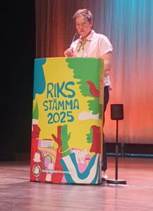 Kvinna står bakom talarstol och ger ett anförande.