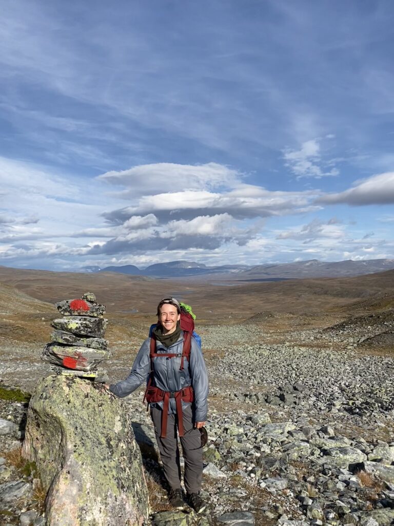 Kvinna på vandring i stenigt landskap, ler kisande mot kameran